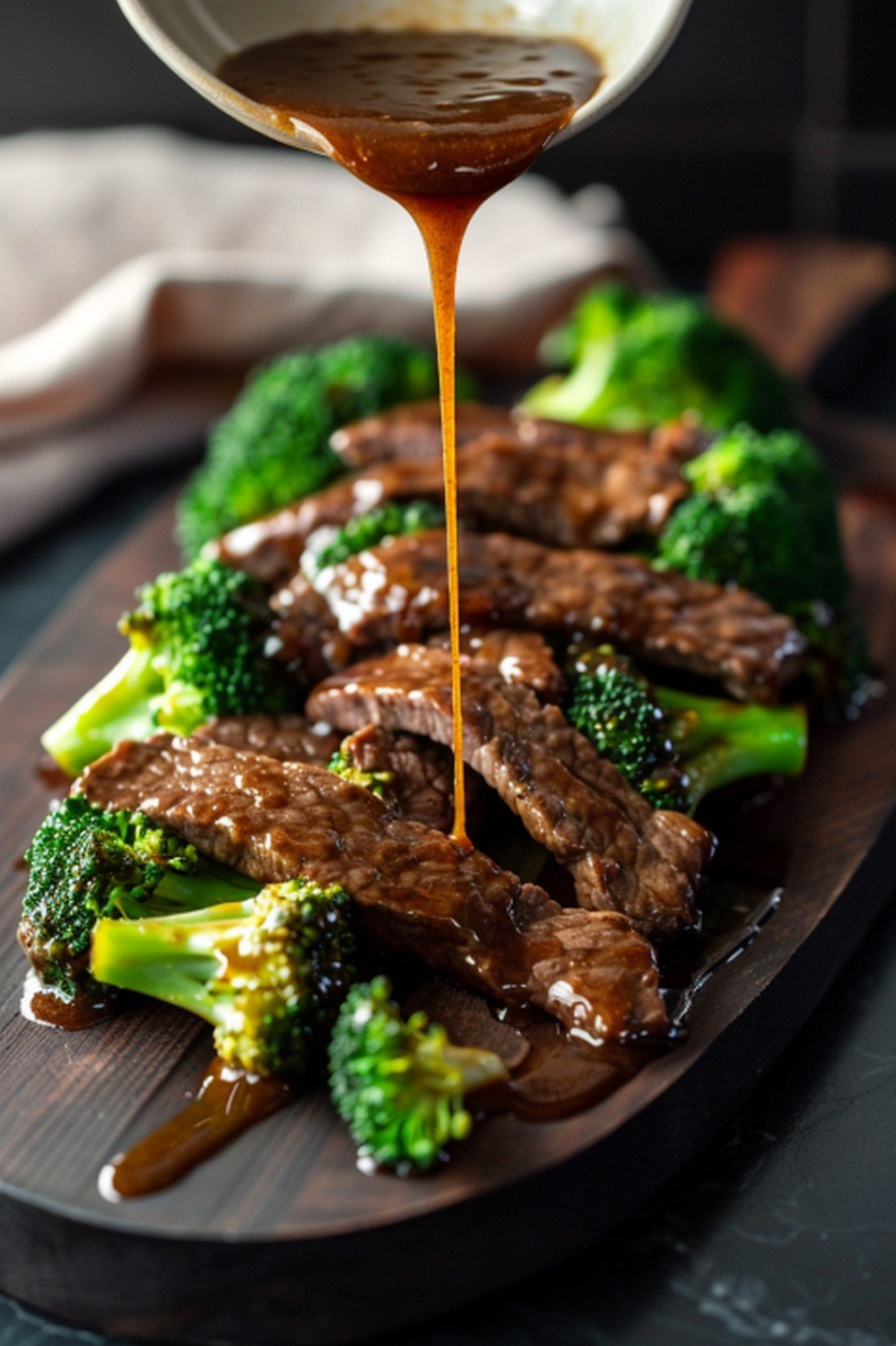 Garlic ginger beef rice bowl with dark glossy sauce ramekin ginger root and chopsticks on stone counter
