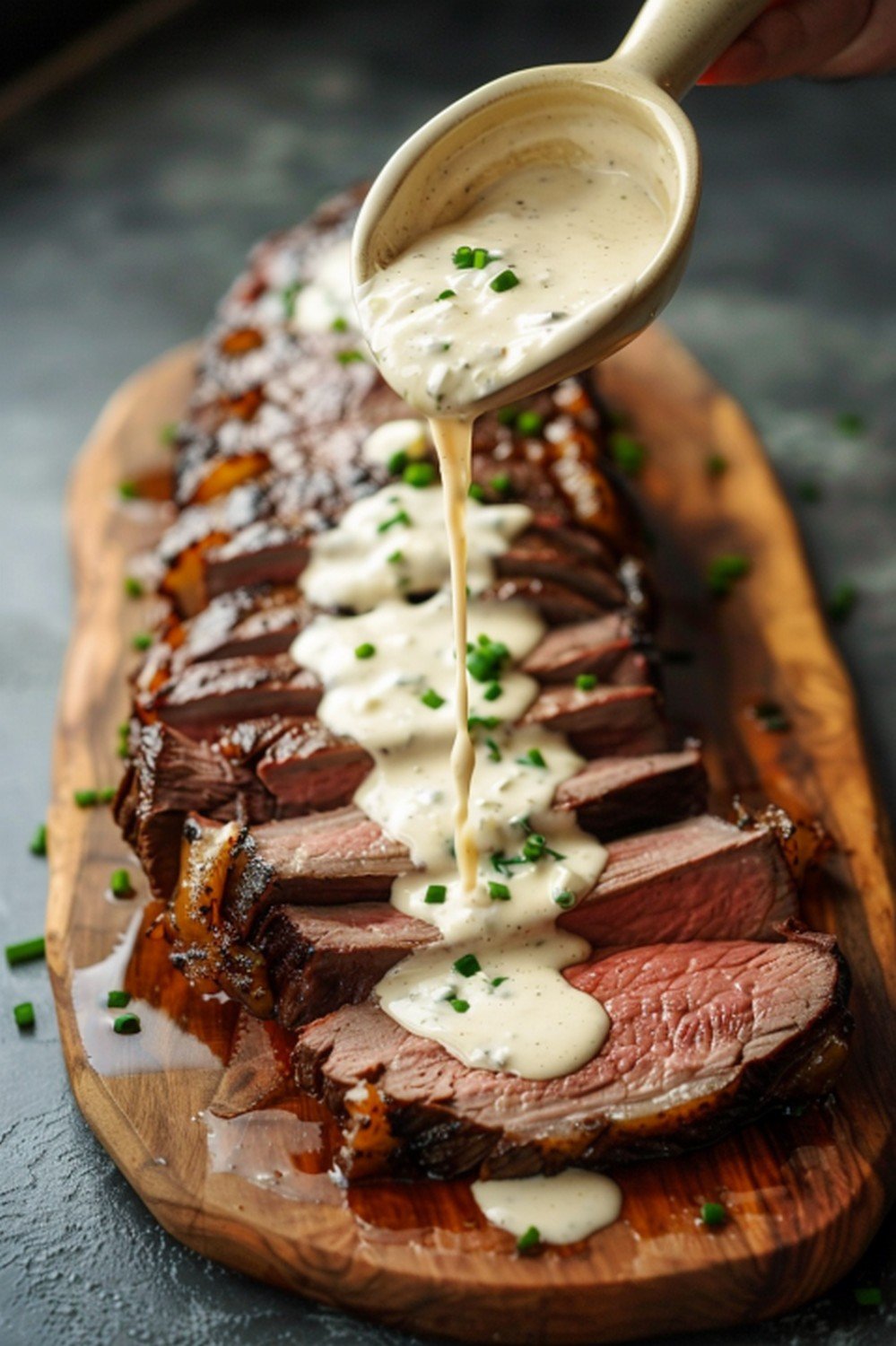 Bright white horseradish cream sauce drizzled from ceramic spoon in slow arc landing on sliced prime rib resting flat on wooden board
